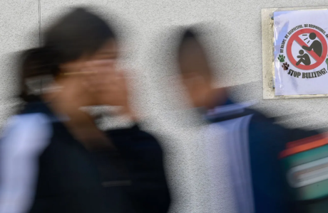 Blurred photo of two students walking by anti-bullying poster in a classroom.