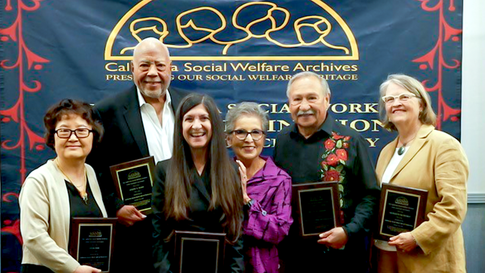 Two men and four women holding awards in front of banner