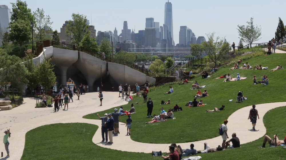 People sitting on the grass and strolling around Little Island Park in Manhattan on a sunny day.