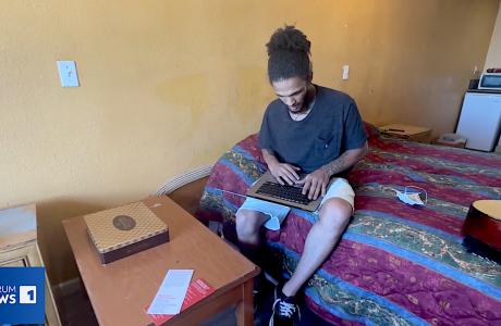 Man on bed in hotel room, typing on laptop