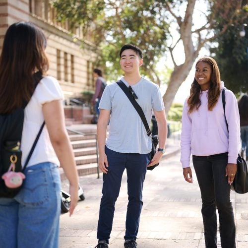 One student has back towards the camera and two students smile at her, in front of Royce Hall at UCLA