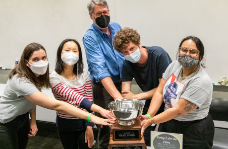 four students and a professor touch the trophy given to the winning team