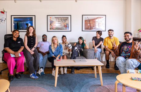 wide angle shot of a living room with people sitting across a couch on chairs facing the camera. theresa willmott-mcMahon sits on the side with her colleagues at her summer internship with Young People to the Front.|headshot of theresa willmott-mcmahon|Theresa stands in a room speaking in front of a group of colleagues at her summer internship.