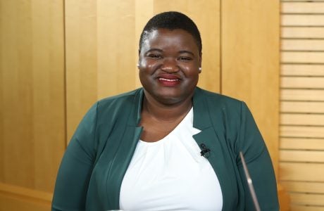 Tierra Bills stands at a podium wearing a white top and green blazer