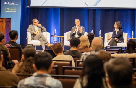 3 panelists speak in front of an audience on stage.|||
