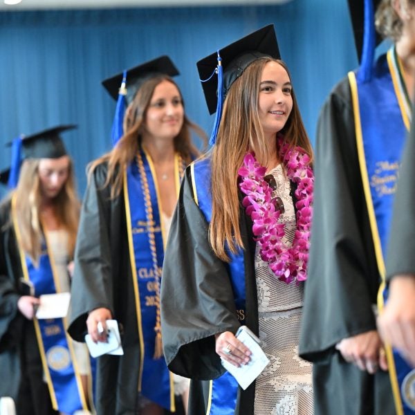 Row of undergraduate students walking down aisle in gowns and cap at Luskin graduation 2026.