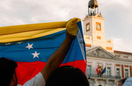 Photo of a man raising up the venezuelan flag in front of a political building in venezuela.
