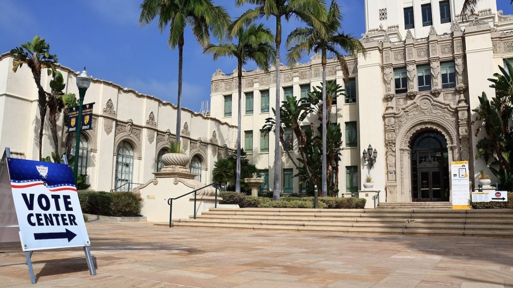 Vote center sign in front of ornate building and palm trees||