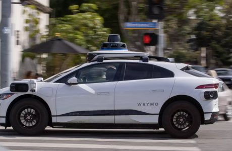 a white driverless vehicle is shown from the left side sitting on a city street