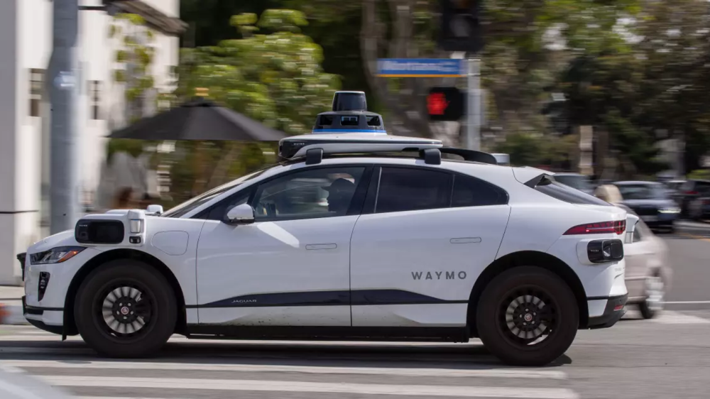 a white driverless vehicle is shown from the left side sitting on a city street