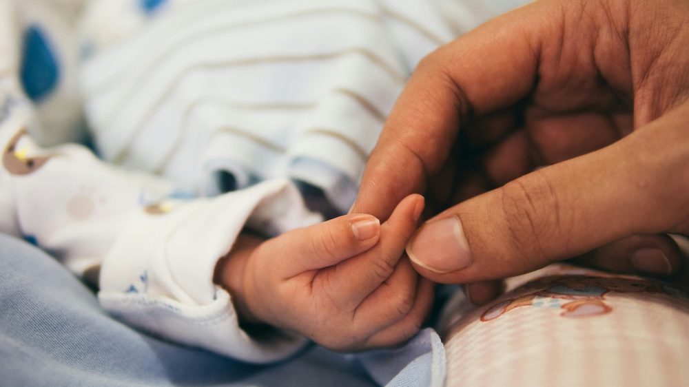 infant hand held by adult hand