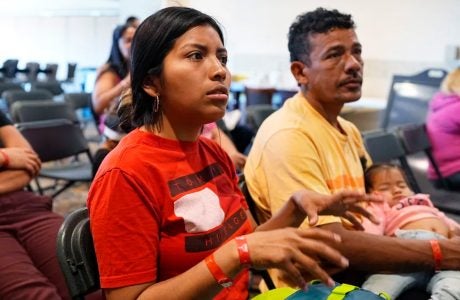 two adults and an infant sit in chairs at an orientation for new immigrants