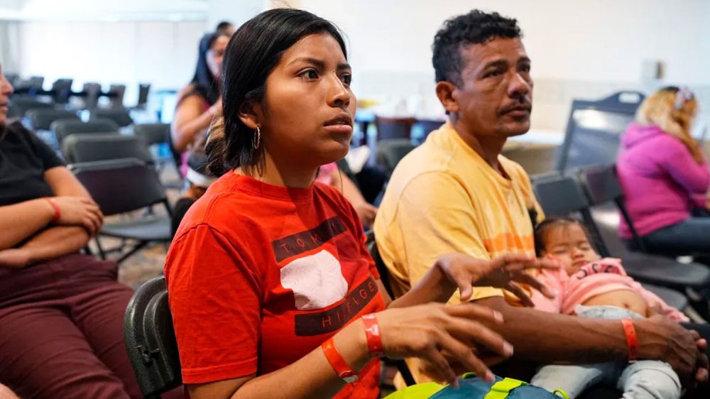 two adults and an infant sit in chairs at an orientation for new immigrants