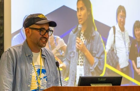 Man in ballcap at podium in front of screen