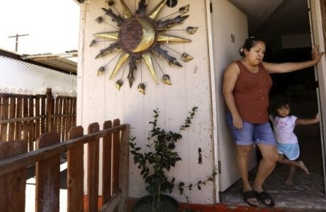 A mother and her daughter lean against the doorframe of their front door on a hot day.