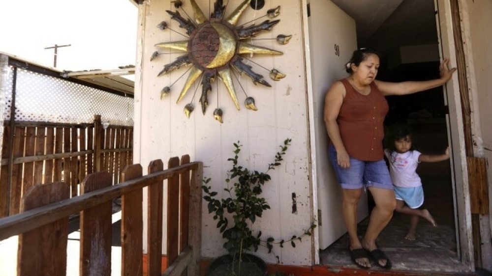 A mother and her daughter lean against the doorframe of their front door on a hot day.