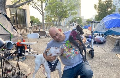 Man smiles and poses crouched down with two dogs