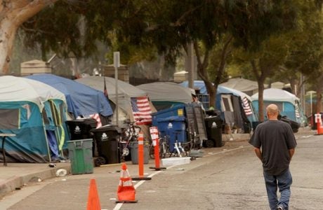 A man walks along the road next to a cluster of tents at a homeless encampment.