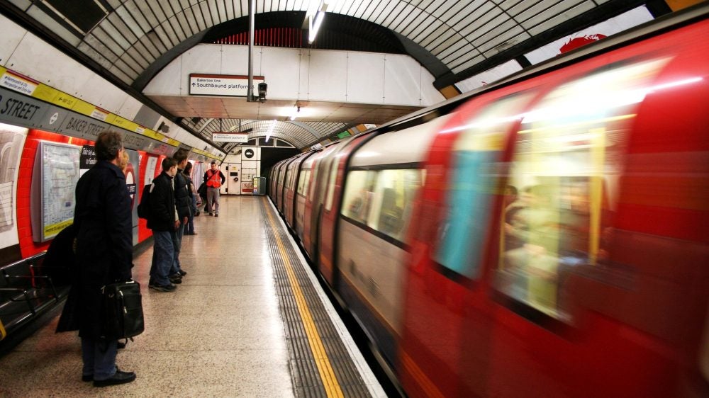 Passengers wait in the subway station for the train, blurry photo of a subway train moving on the right while passengers stand on the left.