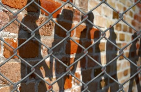 Shadows of people on a wall behind a fence
