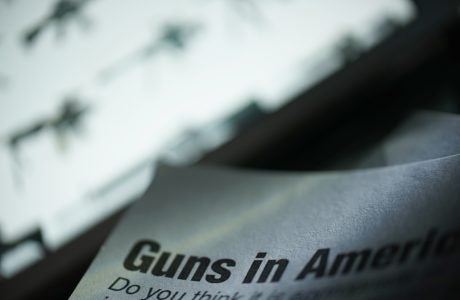 paper shows text reading guns in America in front of a bright screen with images of firearms
