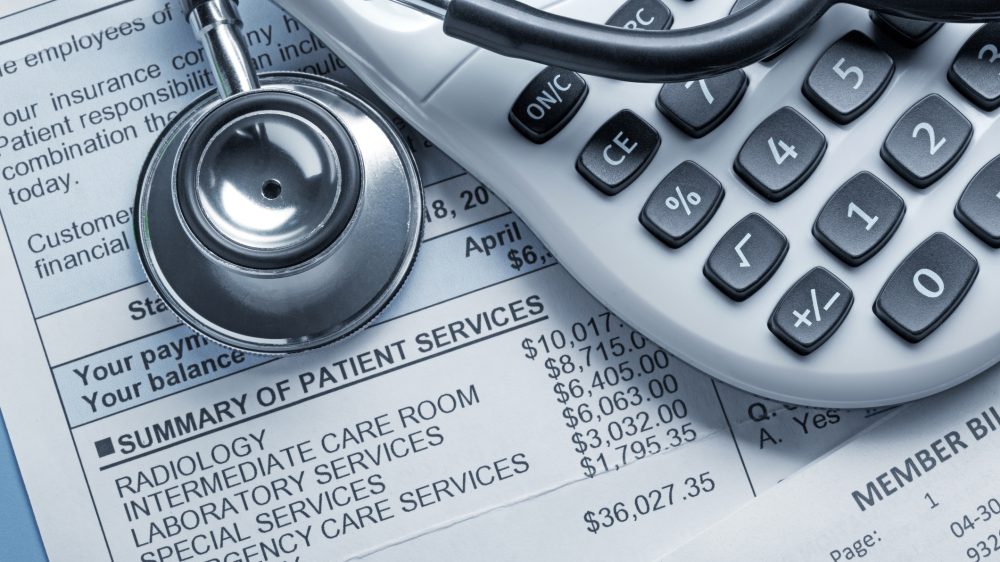 A stethoscope and a calculator rest on top of a medical bill.
