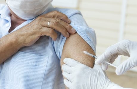 Senior man wearing a protective face mask is getting vaccination from a person with white surgical gloves.