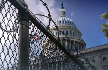 view of the U.S. Capitol Building at an angle behind razor wire fencing with clouds in the background.