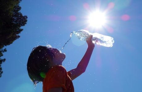 Child outdoors pouring water on self.