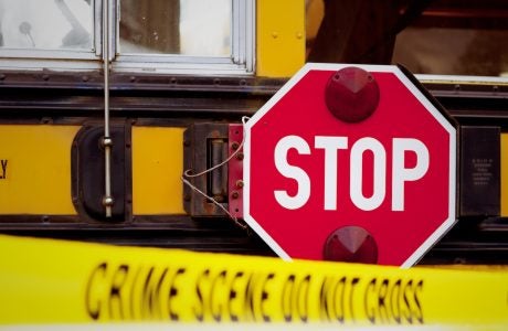 The side of a school bus with cordon tape that reads "CRIME SCENE DO NOT CROSS".
