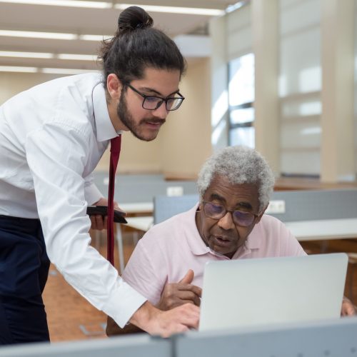 A young man helps a senior citizen in a classroom setting