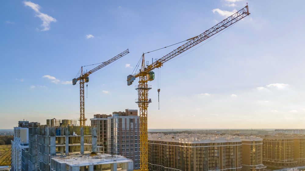 Cranes on the construction site surrounded by new real estates. Scenic aerial photo of growing city districts