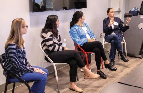 four women are seated in chairs, with three listening as the fourth on far right gestures while talking|portrait photo of Amanda Morrall|portrait photo of Leslea Meyerhoff