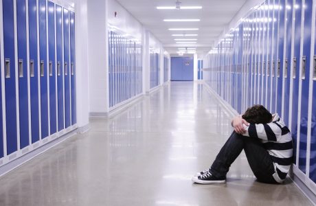 boy sitting with head in hands in school corridor amid blue lockers