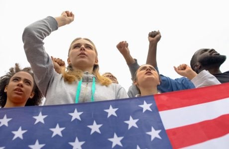 four youth protesting, U.S. flag in foreground