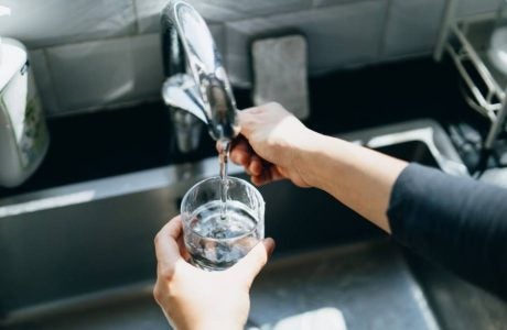 hands turn faucet to run water into a glass