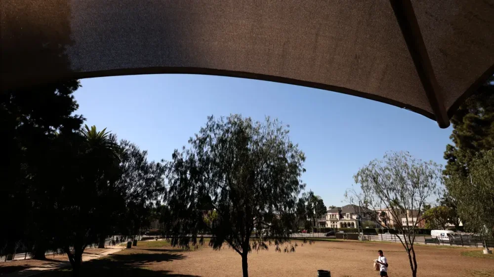 A man heads toward shade at the Hoover Recreation Center, where the playground is draped with a shade canopy.